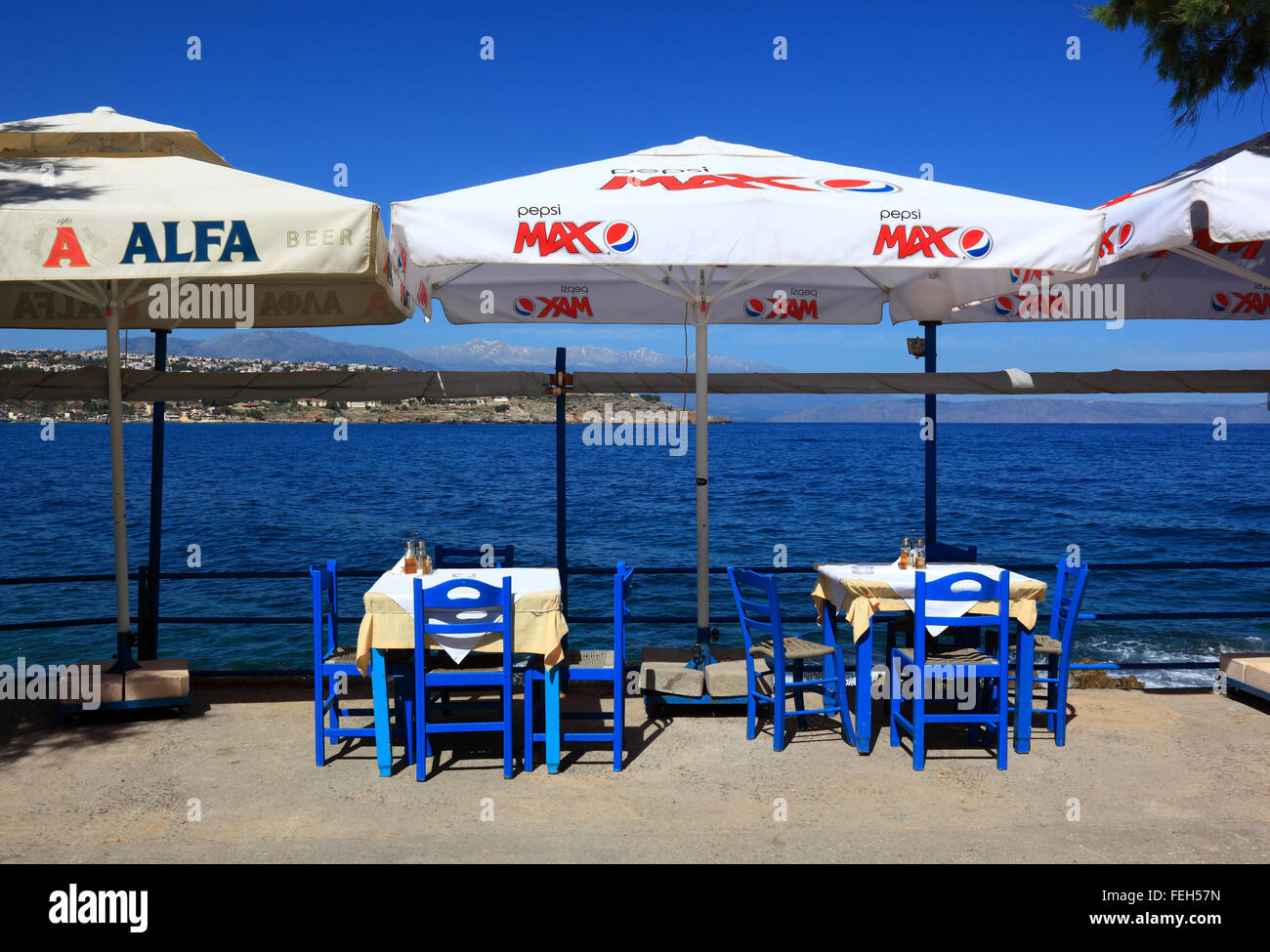 Creta, Rethymnon, street restaurant con sguardo sul mare blu, sedie, tavoli e ombrelloni Foto Stock