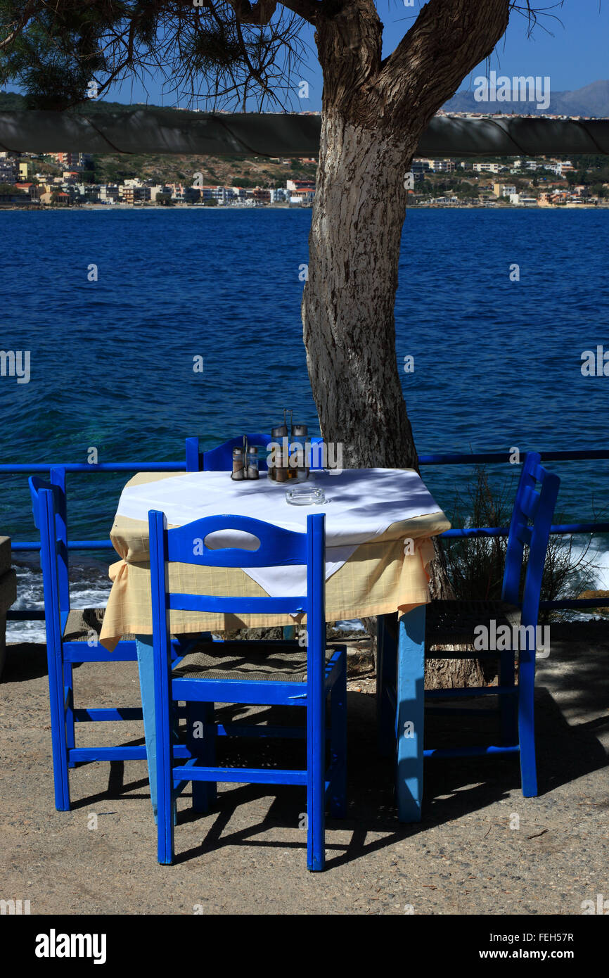 Creta, Rethymnon, street restaurant con sguardo sul mare blu, sedie, tavoli e ombrelloni Foto Stock