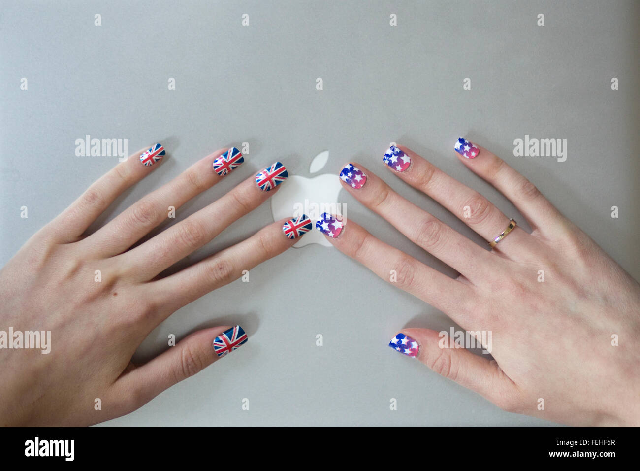 Computer Macbook con le mani con Unione Jack unghie finte e stelle e strisce di chiodi sulla sommità di esso Foto Stock