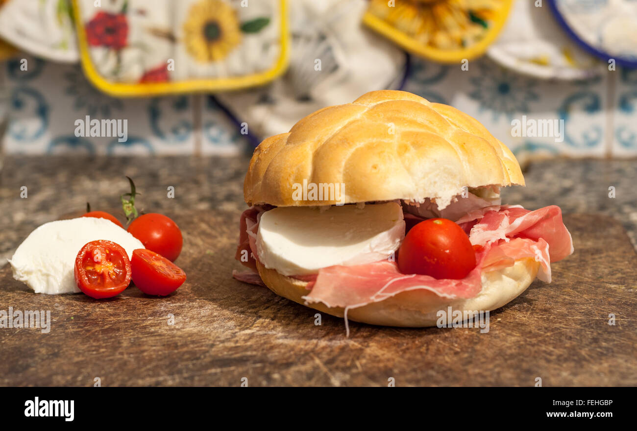 Macro di sandwich al prosciutto, pomodorini e mozzarella su un tagliere di legno Foto Stock