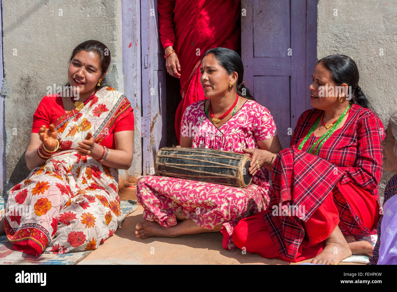 Bhaktapur, Nepal. Donna che gioca un tamburo mentre è seduto con gli amici sul suo portico anteriore. Foto Stock