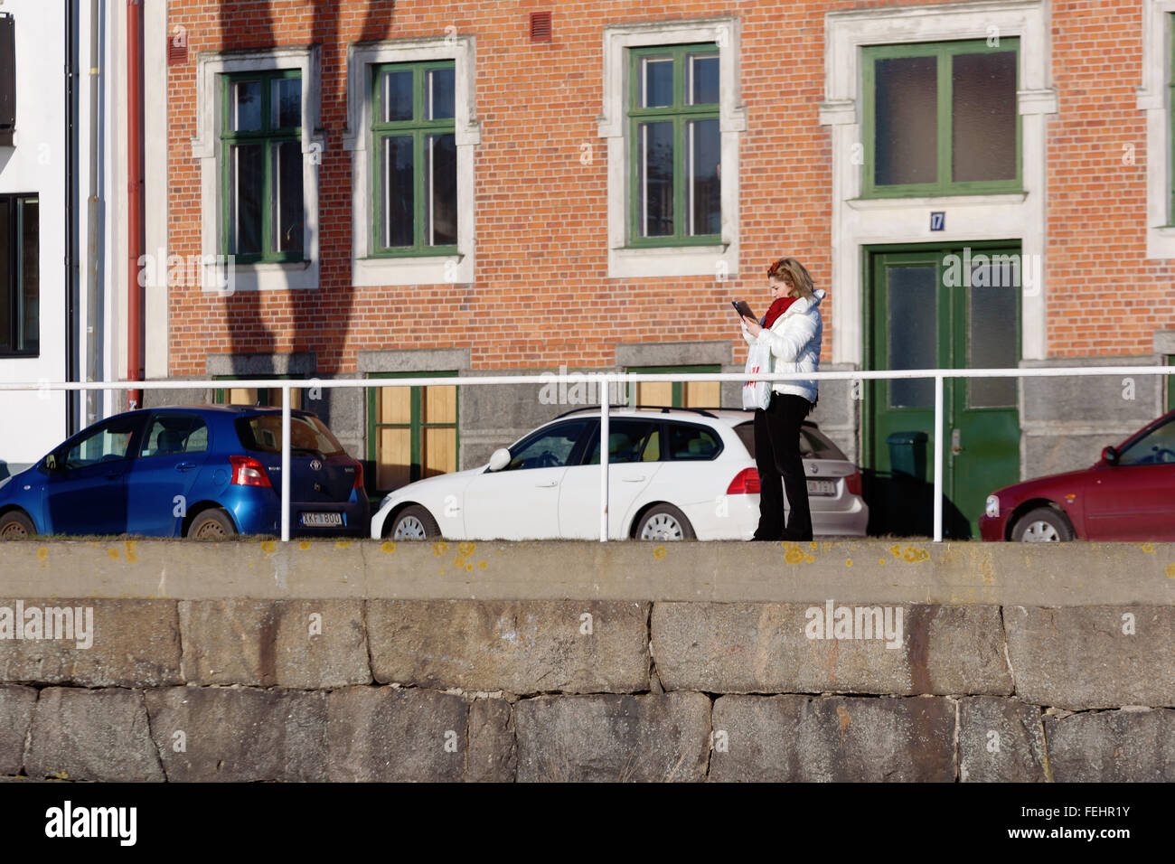 Karlshamn, Svezia - Febbraio 04, 2016: un ignoto femmina è utilizzando il proprio telefono cellulare per scattare fotografie come stand ella al di fuori di una bu Foto Stock