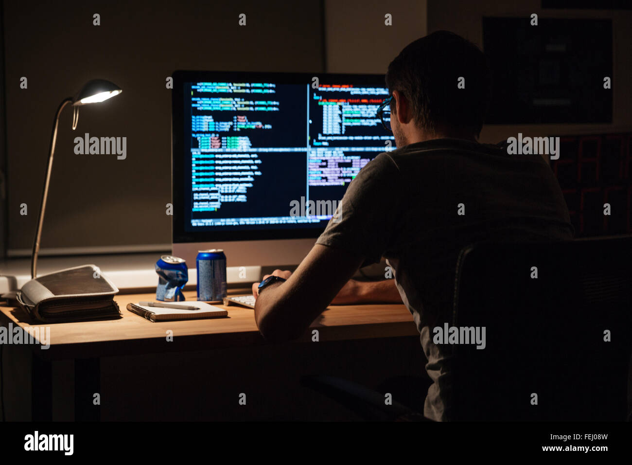 Vista posteriore del programmatore moderno la seduta e la scrittura di codice in dark room Foto Stock