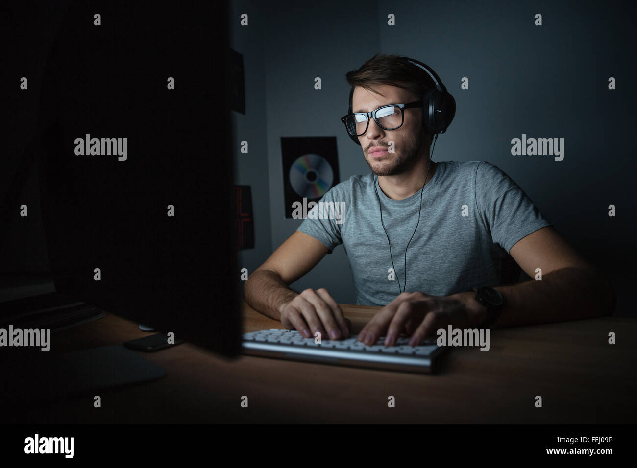 Concentrato giovane cuffie in udienza nella sala buia e uso del computer Foto Stock