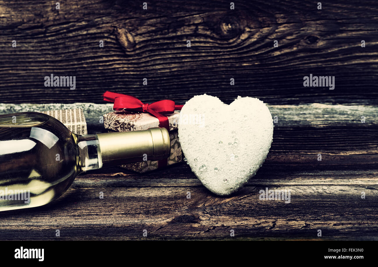 Cuore bianco con gocce di pioggia, bottiglia di vino bianco e confezioni regalo su tavola di legno. Il concetto di amore in stile vintage. Valentines D Foto Stock