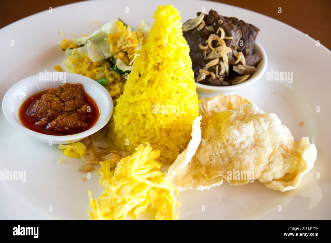 Nasi Kuning indonesiano riso giallo servito con brasato di manzo, shredded uovo, verdure, insalata di noce di cocco, fatti in casa e sambal cracke Foto Stock