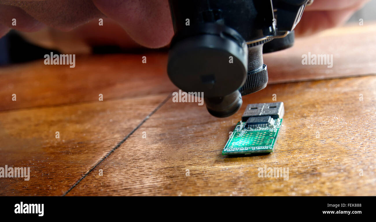 Uomo che guarda gli organi della scheda a circuito stampato tramite uno speciale lenti di ingrandimento Foto Stock