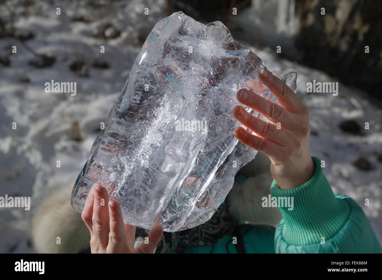 Donna di mani tenendo un grande pezzo di ghiaccio dalla congelati cascata di montagna Foto Stock