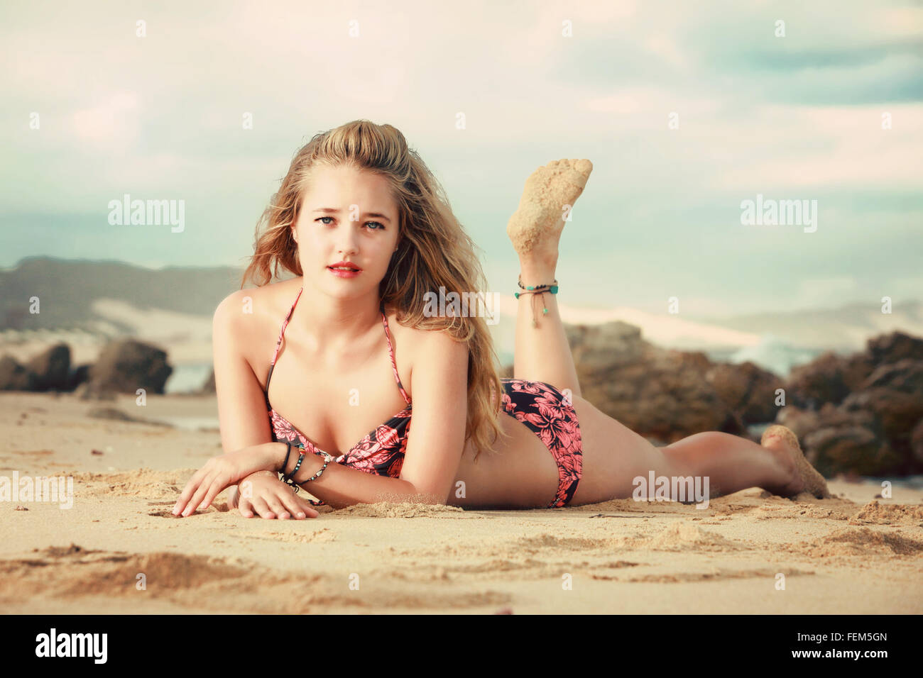 Una bella bionda è sdraiato sul suo stomaco su una roccia sulla spiaggia in Africa. Ella ha un bikini bianco e pantaloni corti, la spiaggia Foto Stock