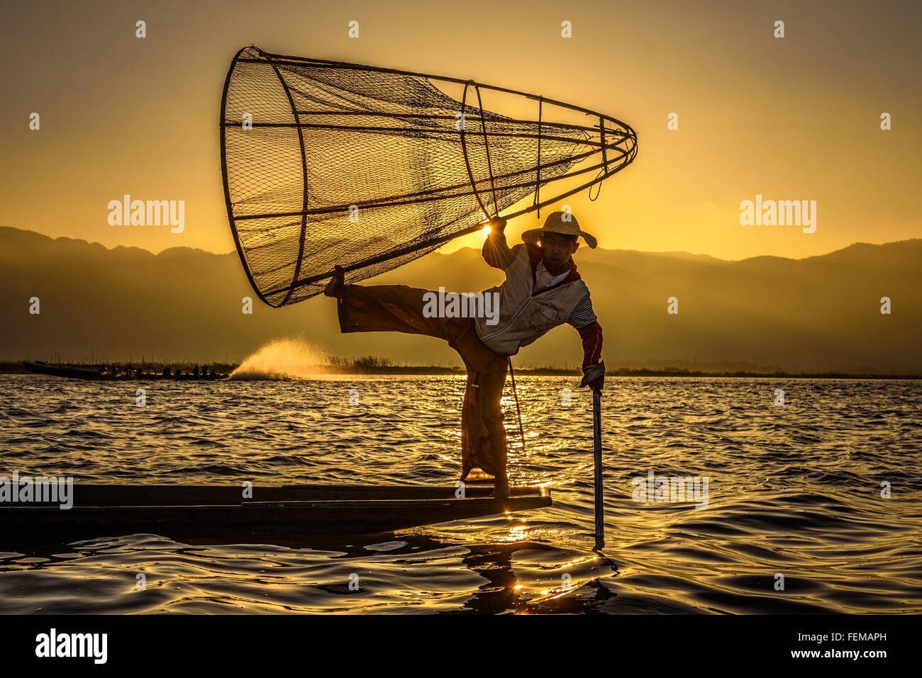 Pescatore birmano su una tradizionale barca di bambù per la cattura di pesce utilizzando una rete di fatti a mano di sunrise Foto Stock