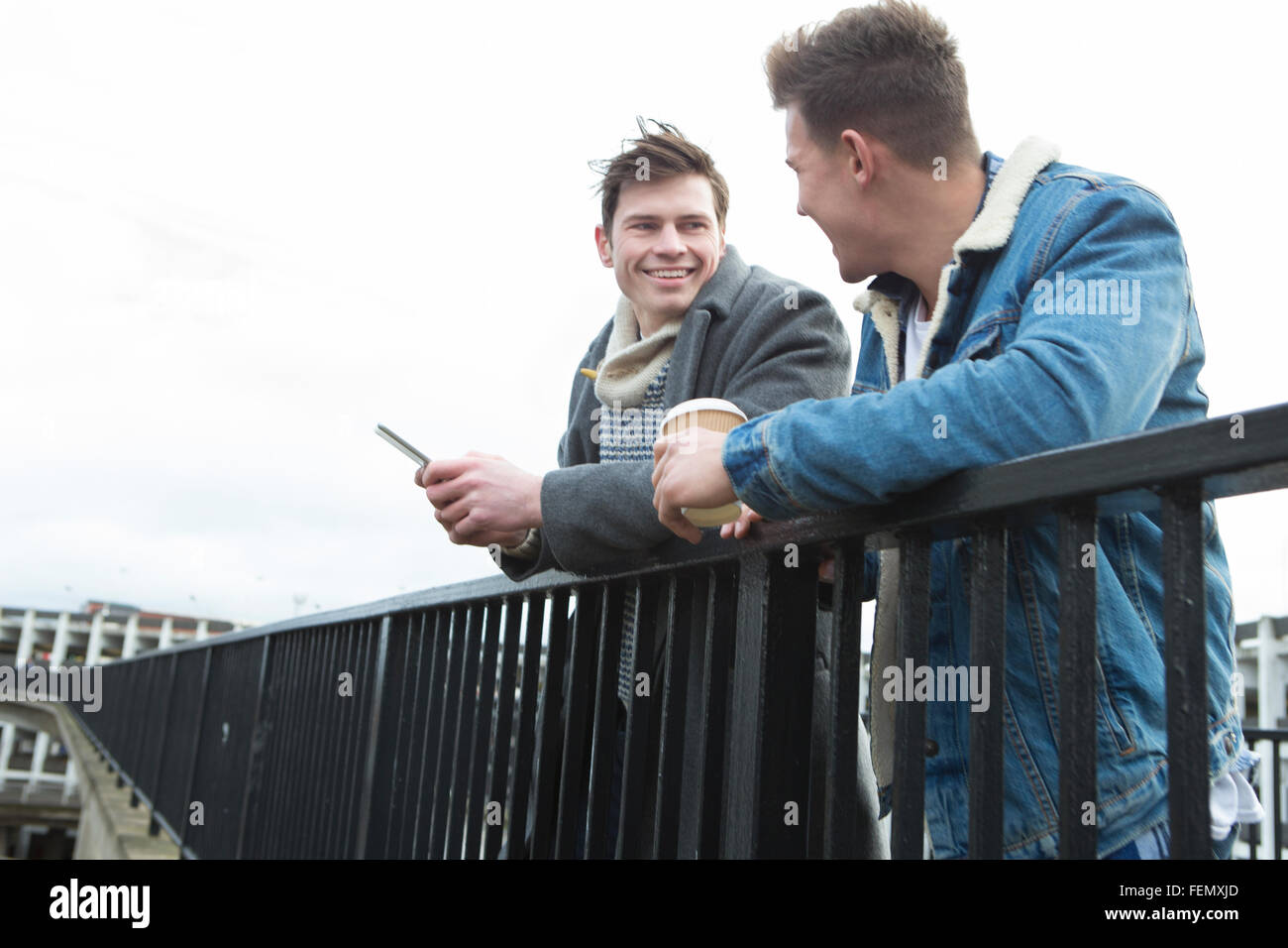 Due giovani uomini che parlano in città. Uno è in possesso di uno smartphone, l'altra è in possesso di un dispositivo monouso Tazze di caffè. Foto Stock
