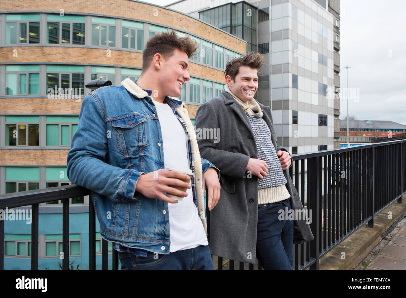 Due giovani uomini che parlano in città. Uno è in possesso di un dispositivo monouso Tazze di caffè. Foto Stock