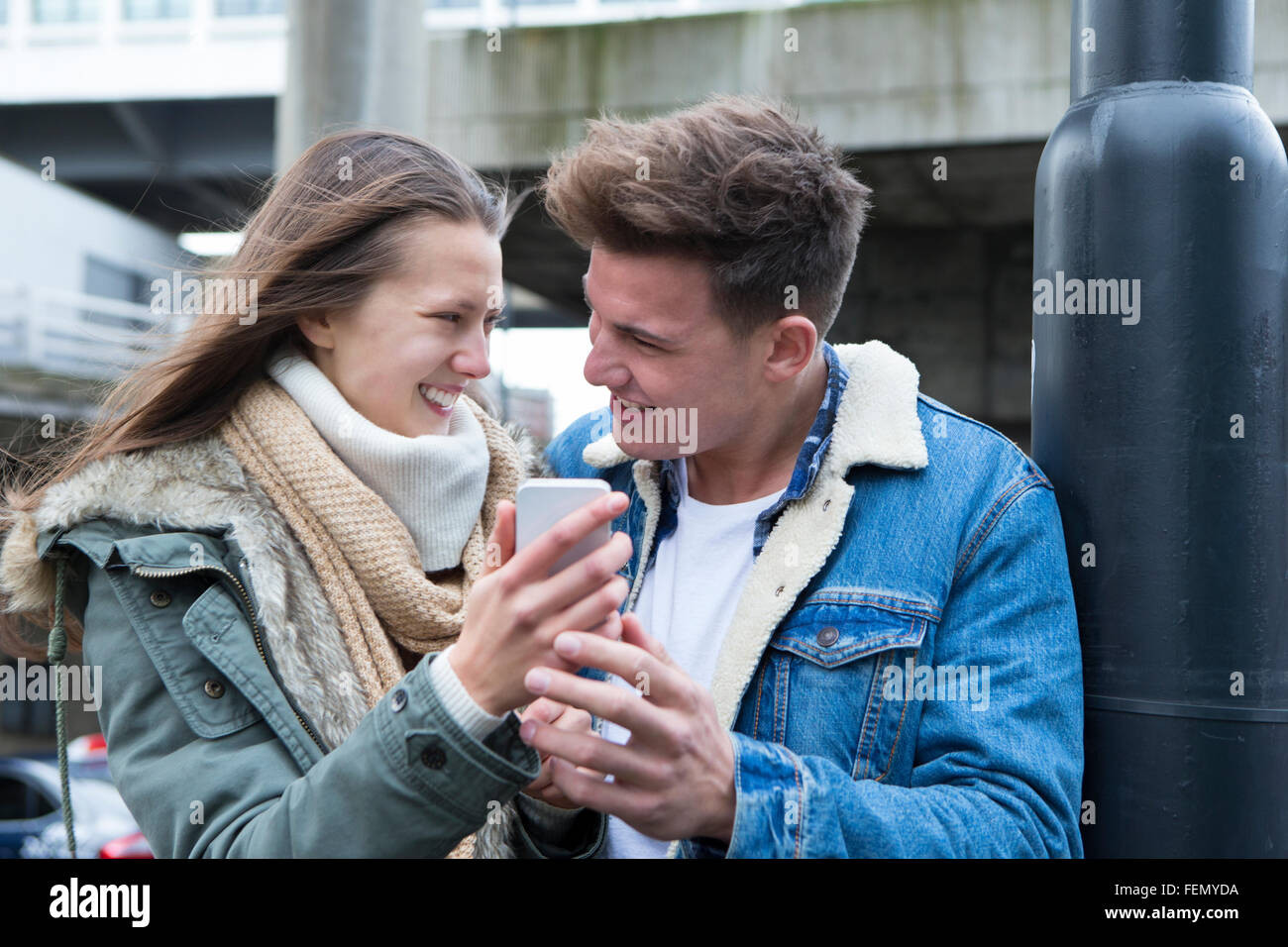 Coppia giovane in piedi insieme nel freddo, guardando uno smartphone insieme Foto Stock