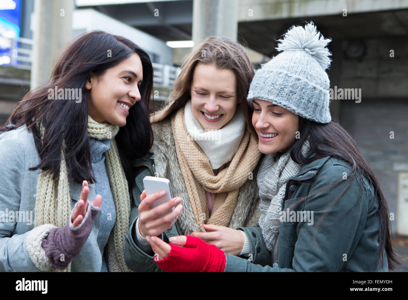Tre giovani donne in città, guardando qualcosa su uno smartphone. Foto Stock