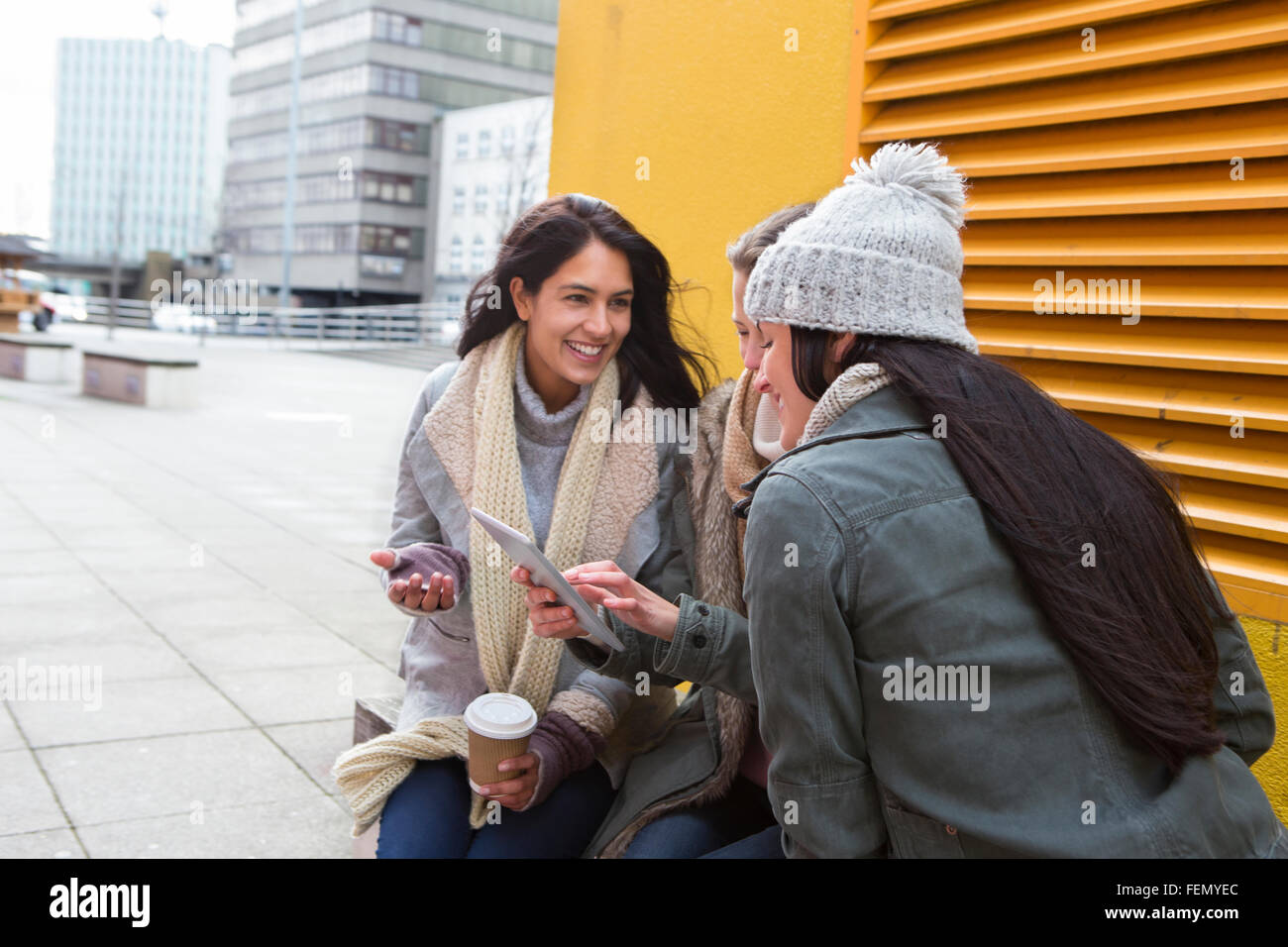 Tre giovani donne sedute in città, guardando qualcosa su una tavoletta digitale. Foto Stock