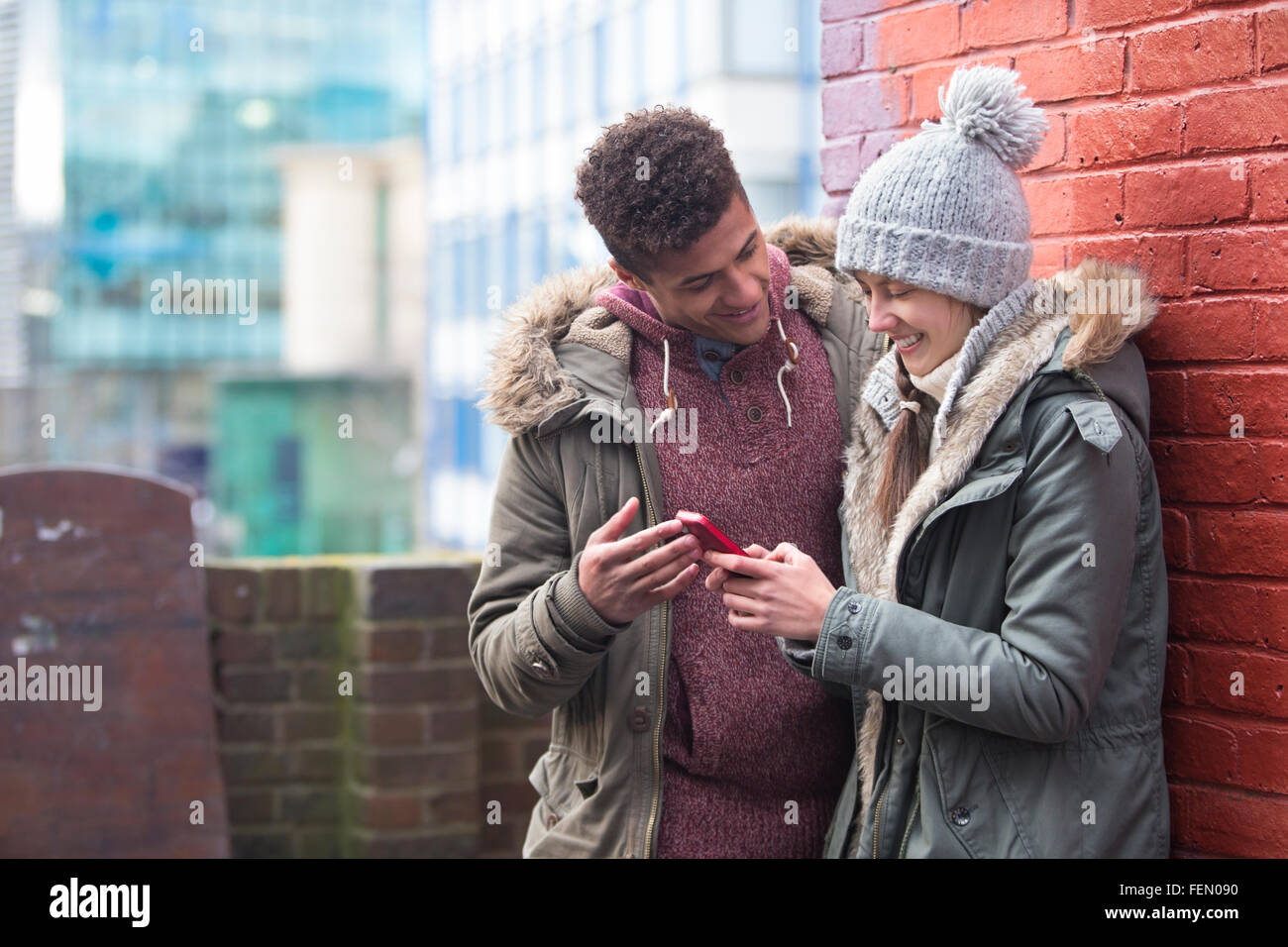 Coppia giovane in piedi insieme nel freddo, guardando uno smartphone Foto Stock
