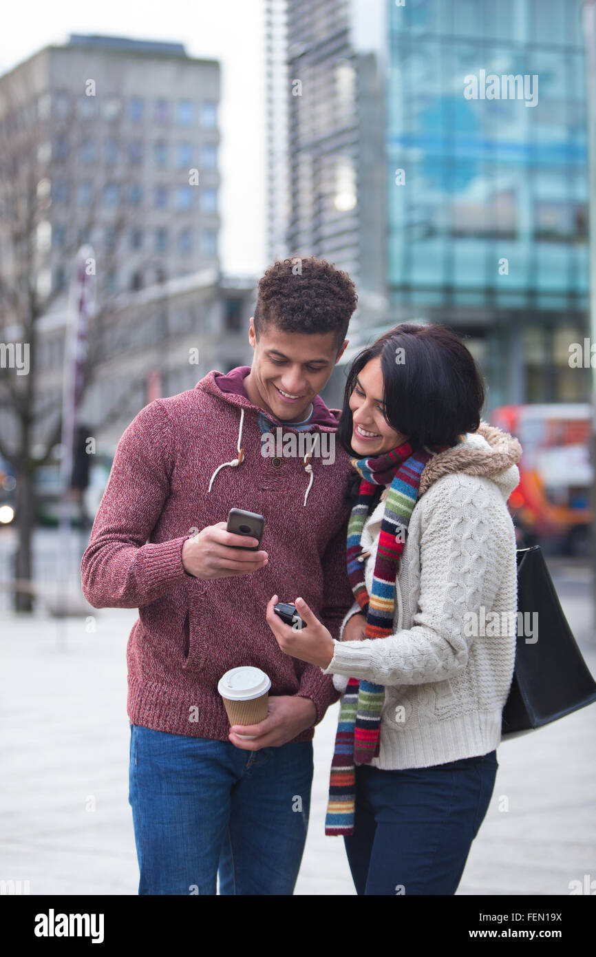 Coppia giovane in piedi insieme nella città, guardando uno smart phone Foto Stock
