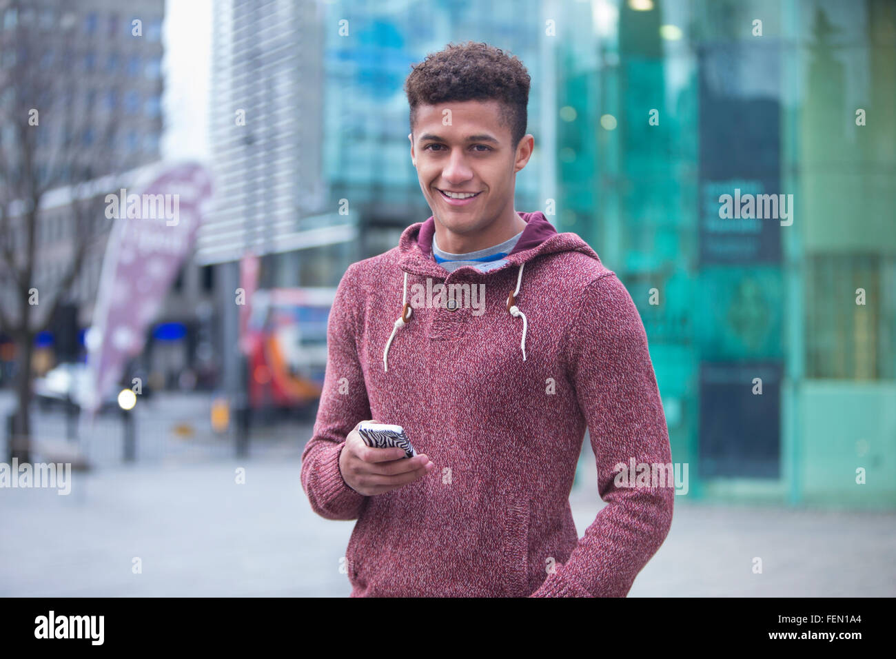 Giovani, mixed-gara uomo in città con uno smart phone. Egli sorride alla telecamera. Foto Stock