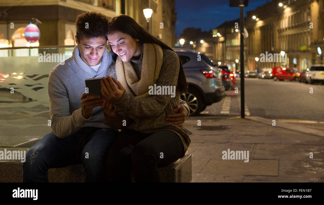 Coppia giovane guardando una tavoletta digitale insieme. Essi sono qui seduti nella città a sera. Foto Stock