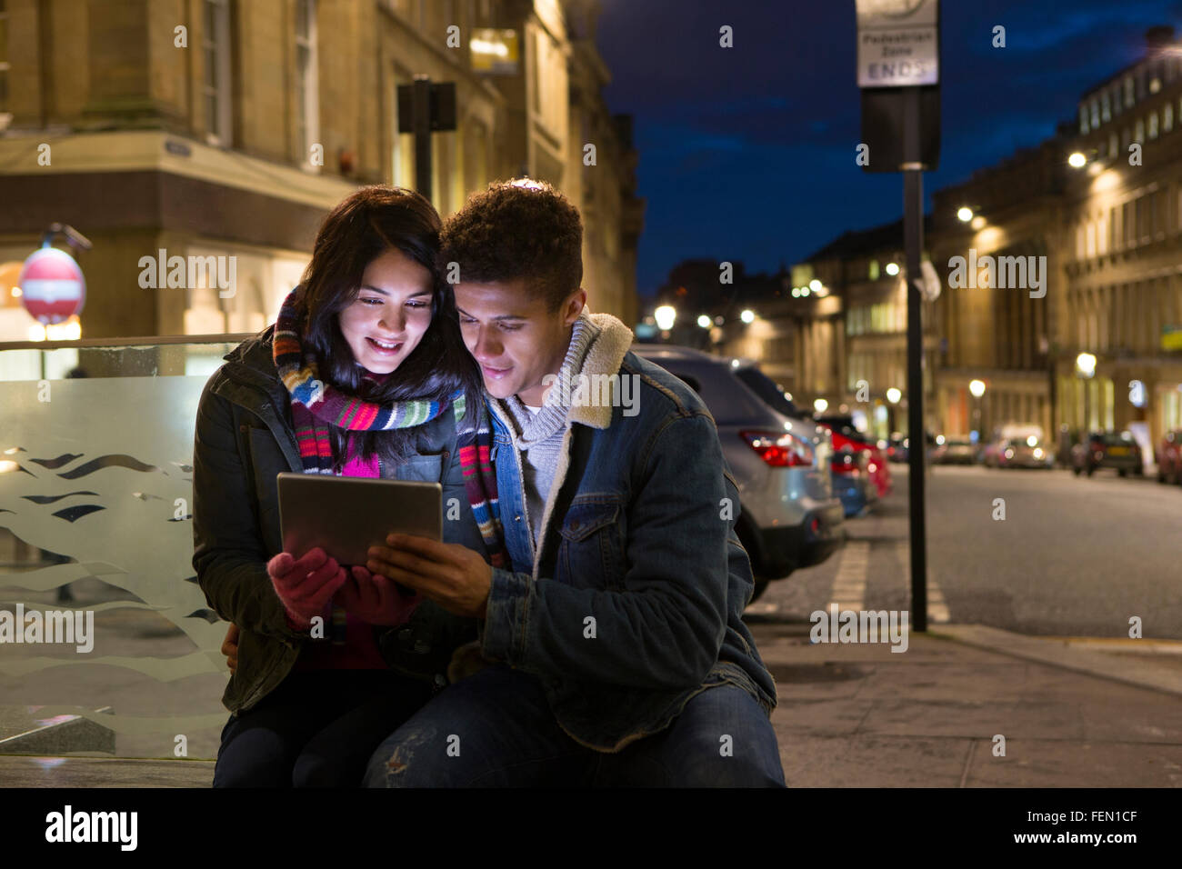 Coppia giovane guardando una tavoletta digitale insieme. Essi sono qui seduti nella città a sera. Foto Stock