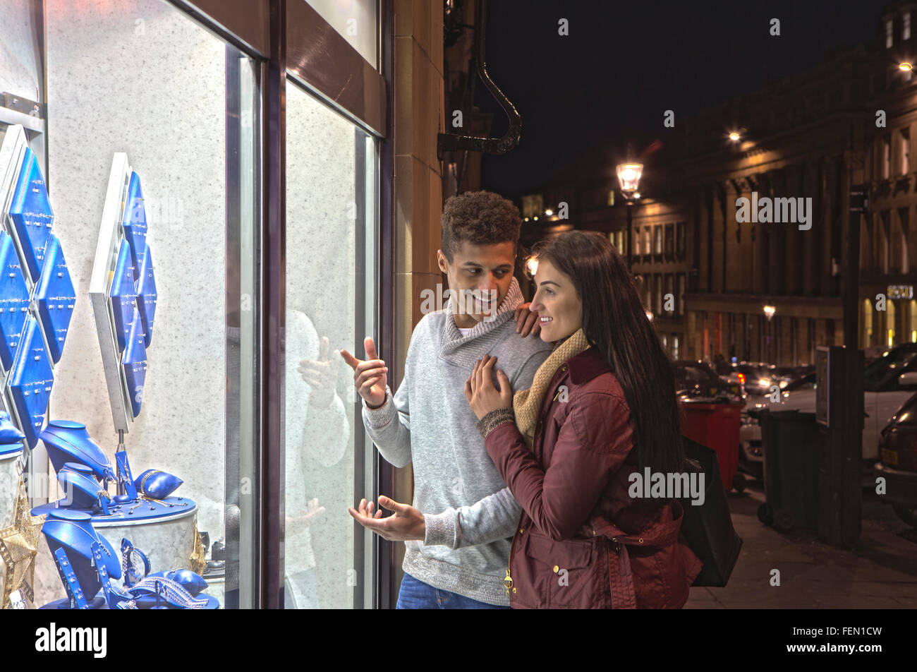 Coppia giovane guardando gioielli attraverso una vetrina in città a sera. Foto Stock