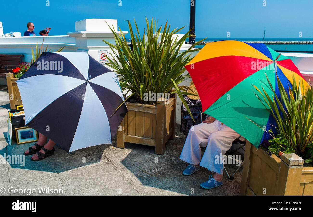 Due donne con grandi ombrelloni colorati seduti sul lungomare a Herne Bay Foto Stock