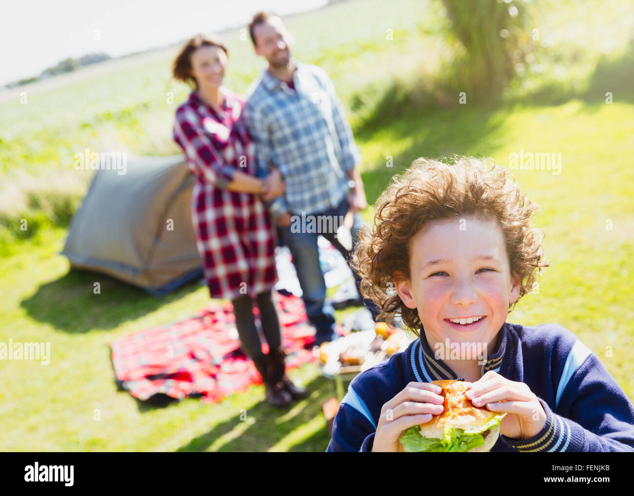 Ritratto sorridente ragazzo mangiare hamburger con i genitori a sunny campeggio Foto Stock