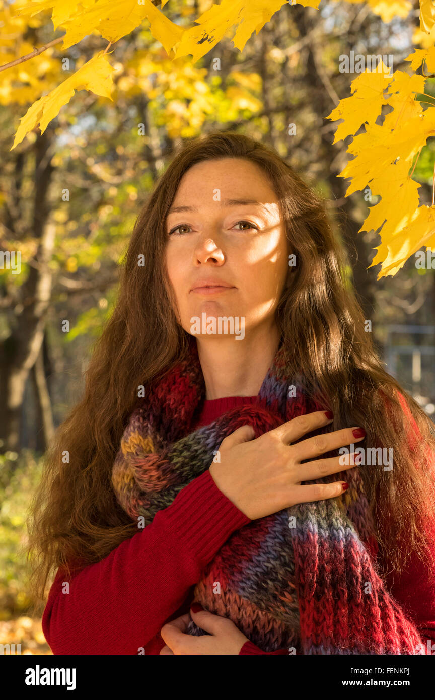 Donna con capelli castani in autunno foresta. Abbraccio con una sciarpa multicolore. Foto Stock