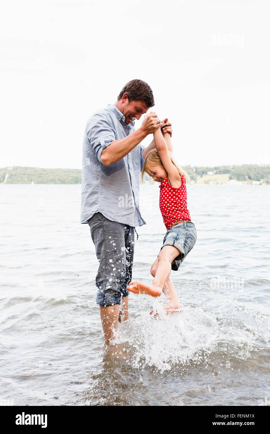 Uomo maturo sollevando la figlia dal lago di Starnberg, Baviera, Germania Foto Stock