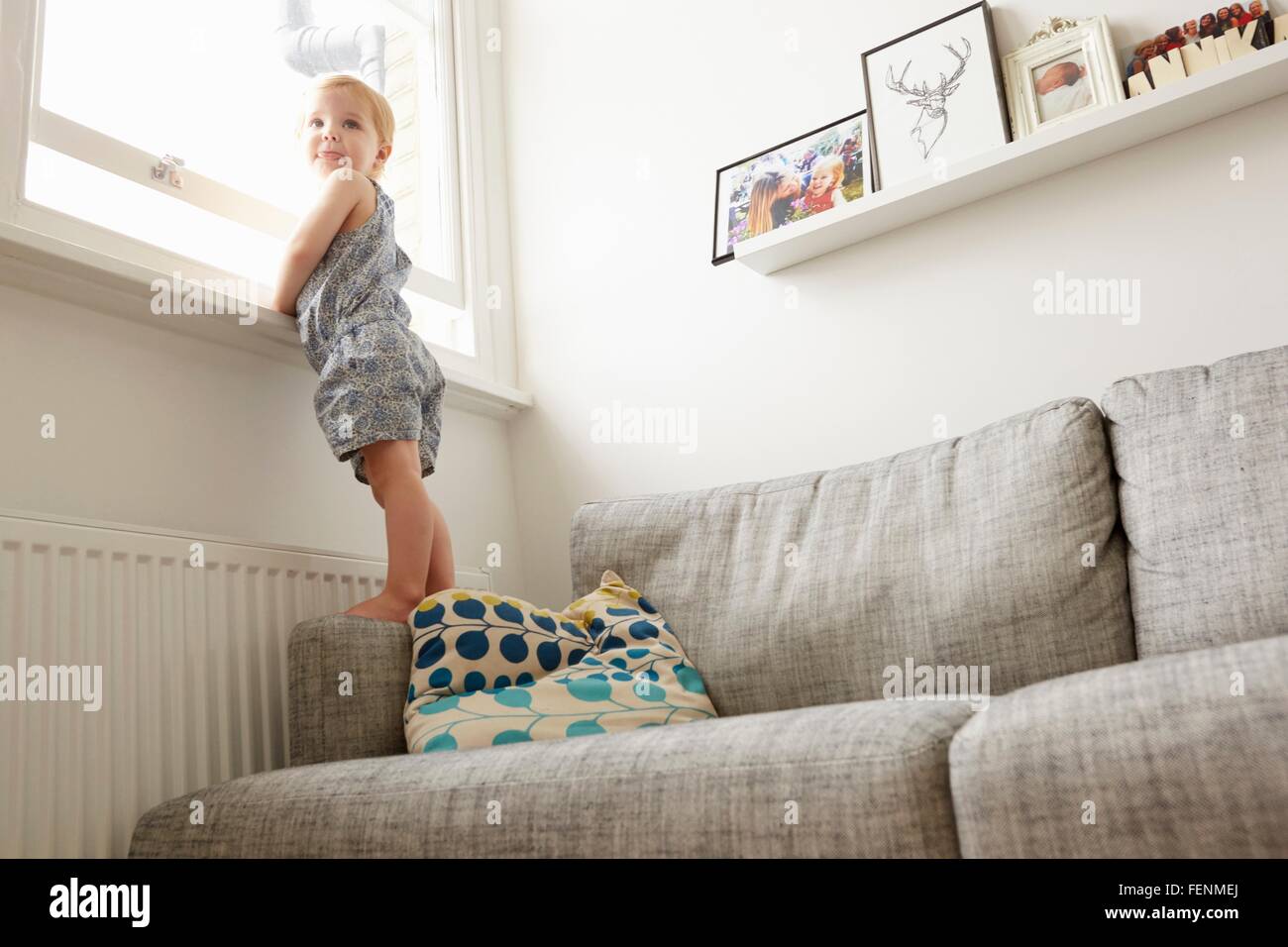 Basso angolo di visione femminile di bambino in piedi sul divano dalla finestra Foto Stock