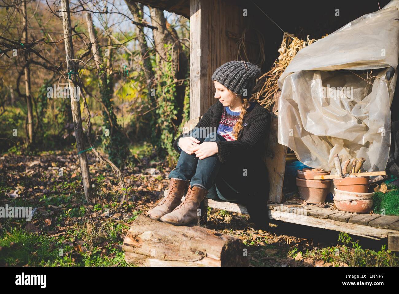 Giovane donna seduta nel Tugurio indossando knit hat guardando lontano Foto Stock
