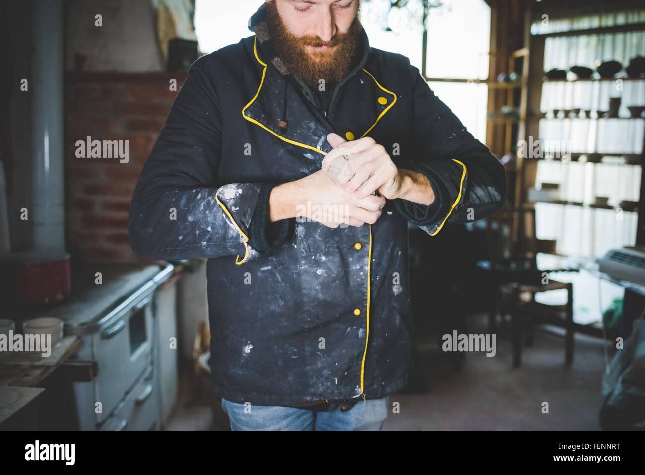 Barbuto metà uomo adulto spremitura di argilla nelle mani, guardando verso il basso Foto Stock