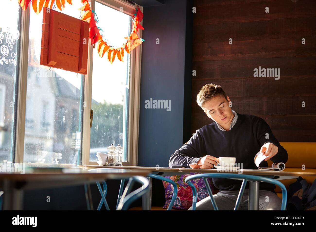 Giovane uomo solo in cafe a bere caffè e la lettura magazine Foto Stock