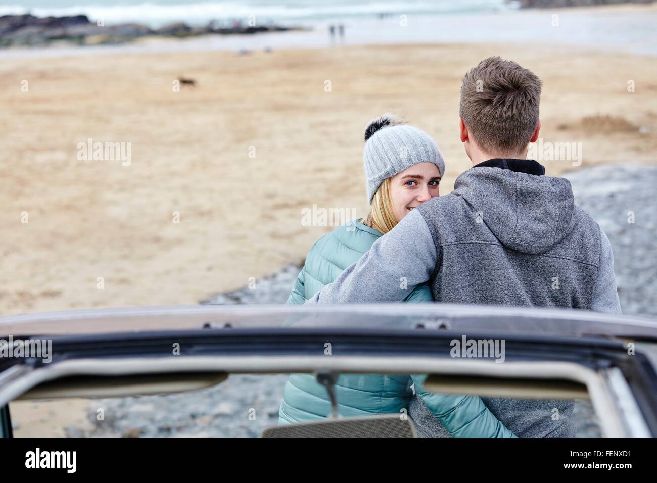 Coppia giovane con le braccia intorno a ogni altro in spiaggia, Constantine Bay, Cornwall, Regno Unito Foto Stock