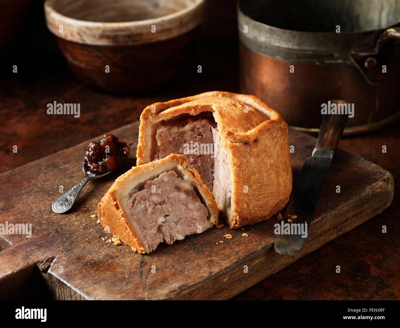 Affettato Melton Mowbray pasticcio di maiale con cucchiaio di sottaceti sul tagliere di legno Foto Stock