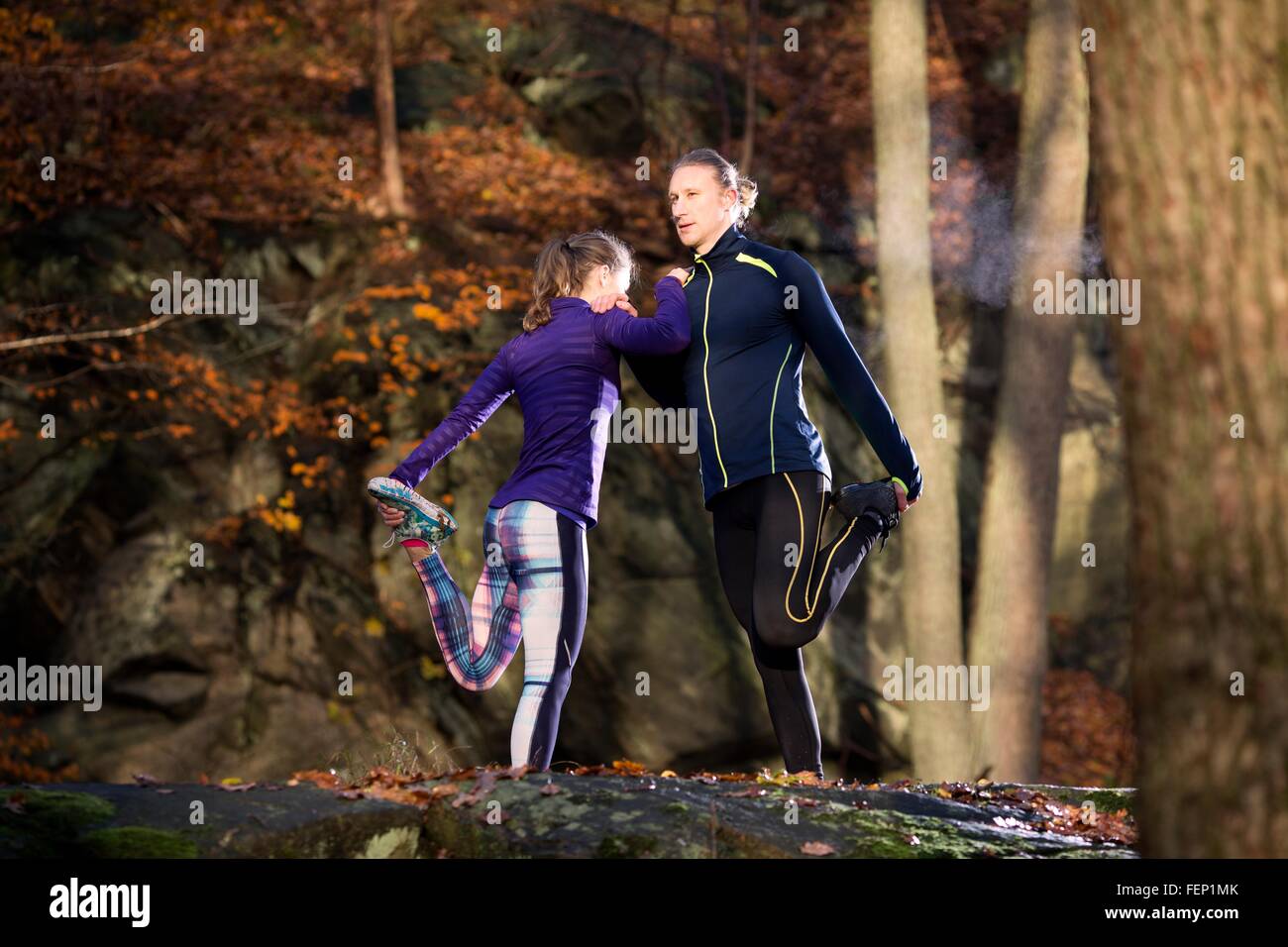 Matura in foresta appoggiata contro ogni altra gamba sollevata tenendo il piede stretching Foto Stock