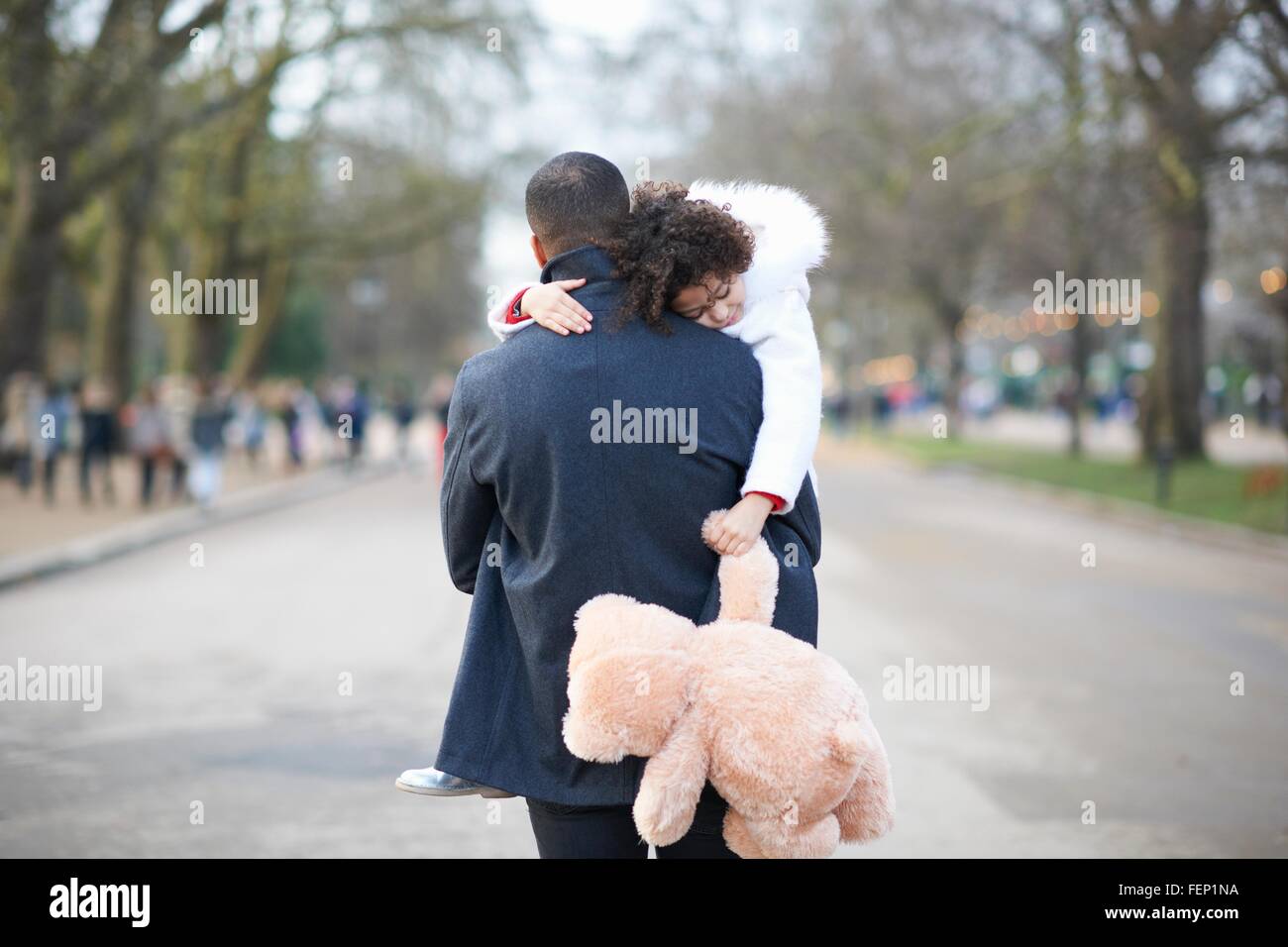 Vista posteriore del padre che porta la figlia a pelo holding peluche Foto Stock