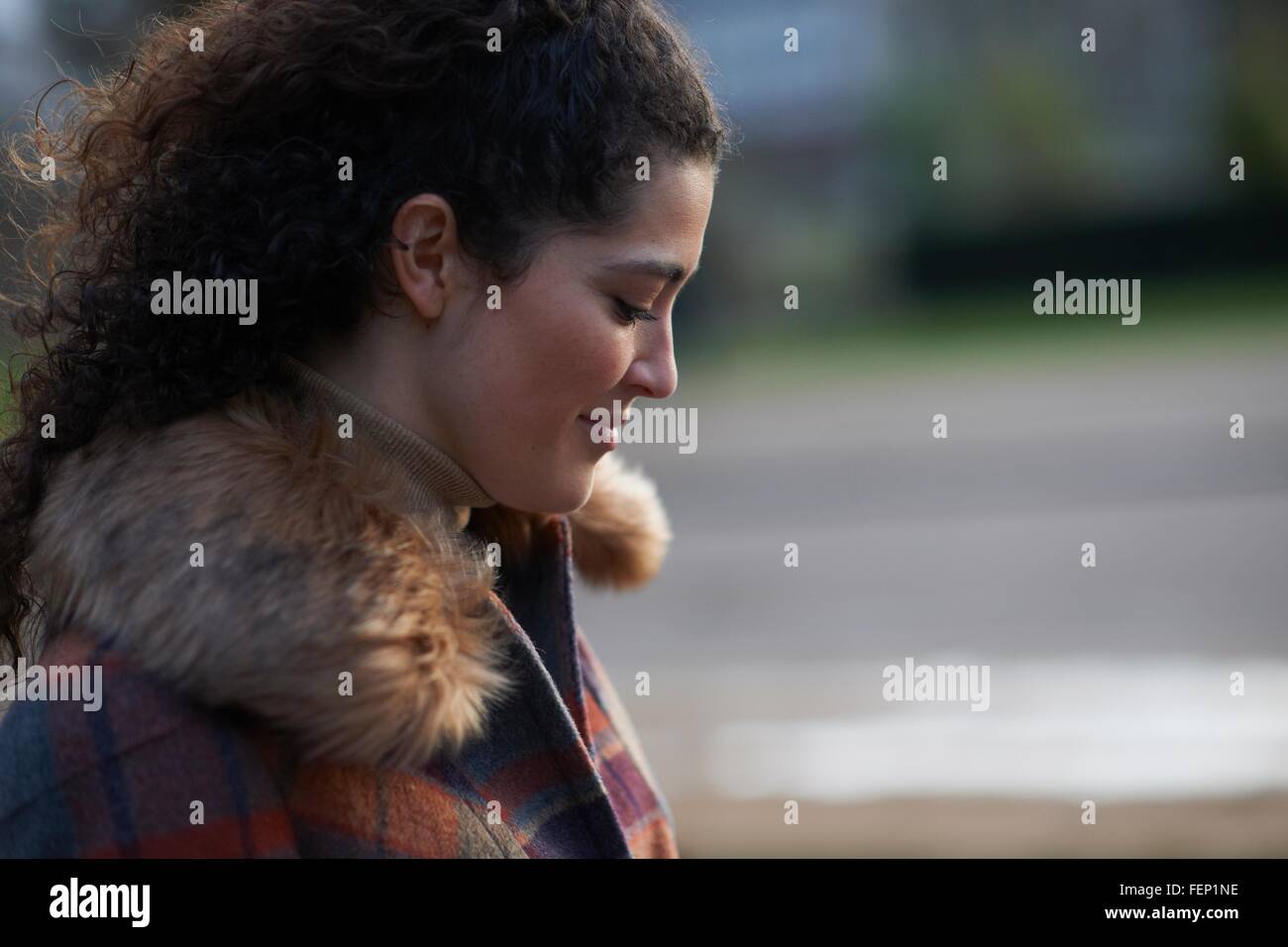 Vista laterale dei capelli ricci donna che indossa tartan rivestimento in pelliccia cappotto guardando giù sorridente Foto Stock