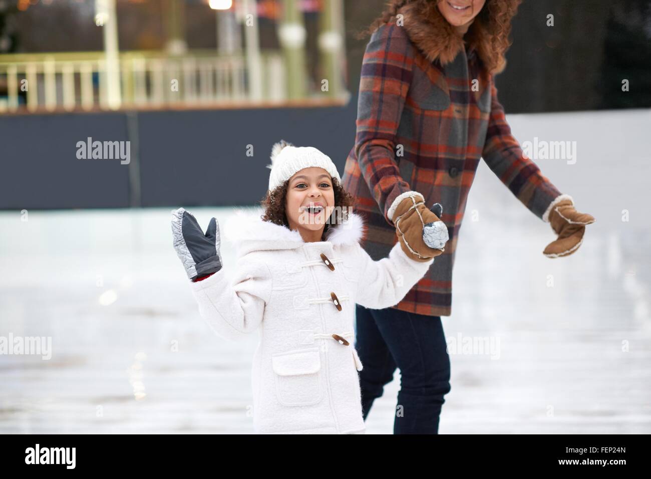 Ragazza il pattinaggio su ghiaccio con la madre, tenendo le mani guardando sorridente della fotocamera Foto Stock