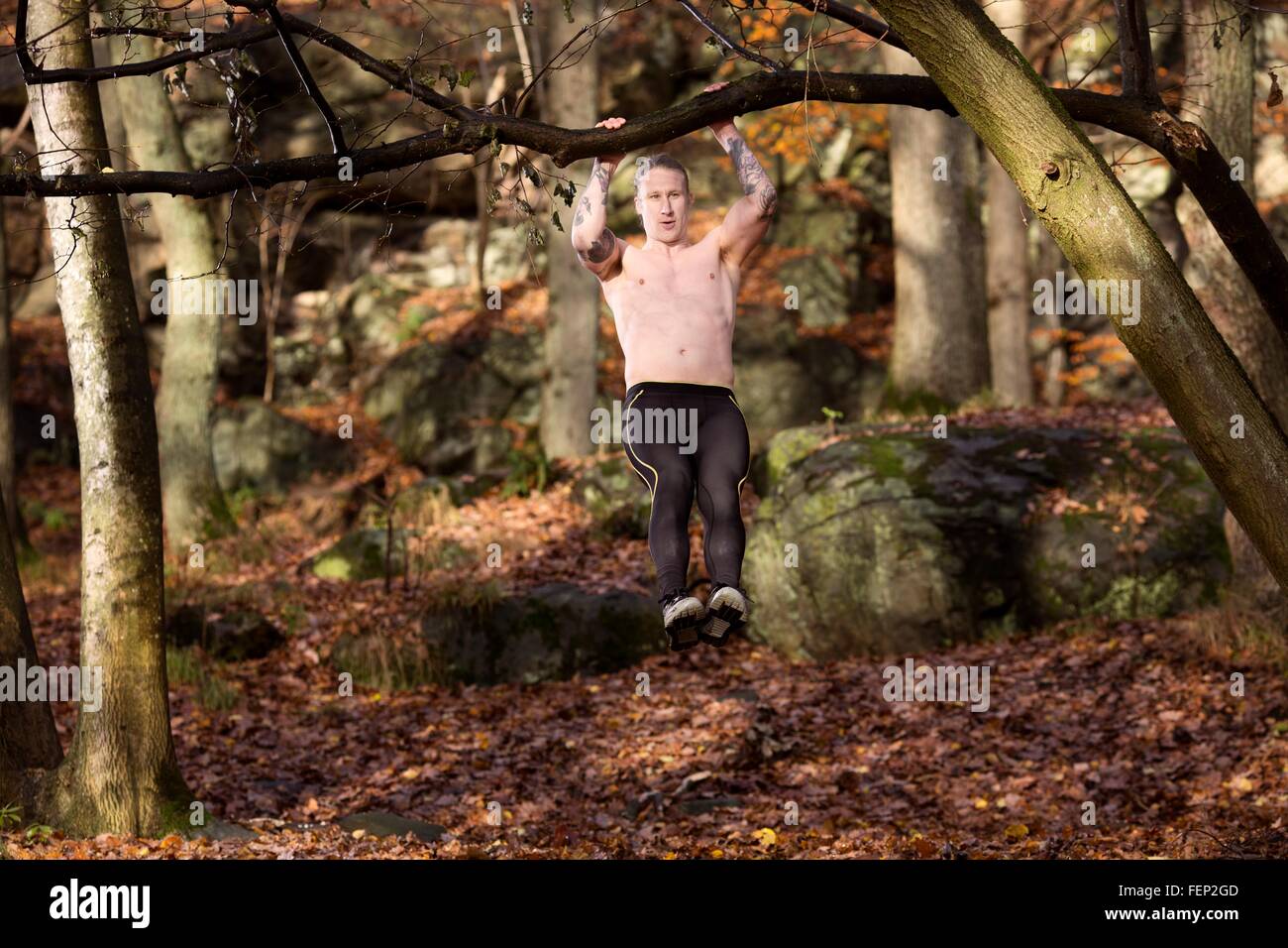 Lunghezza piena vista frontale di tatuati metà uomo adulto nella foresta facendo tirare su albero Foto Stock