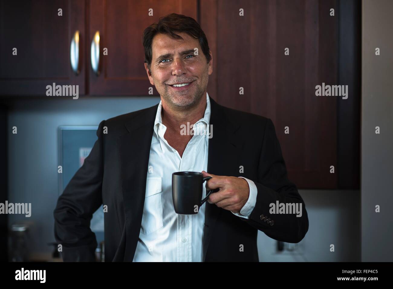 Uomo maturo indossando maglietta e tuta giacca holding tazza da caffè guardando sorridente della fotocamera Foto Stock