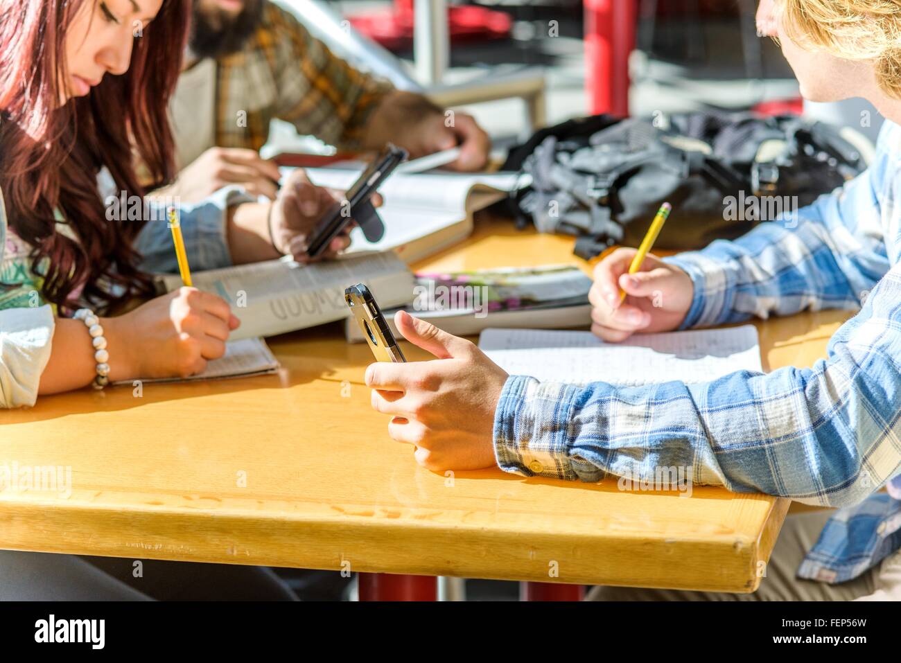 Ritagliato colpo di studenti universitari utilizzando gli smartphone e iscritto alla scrivania Foto Stock