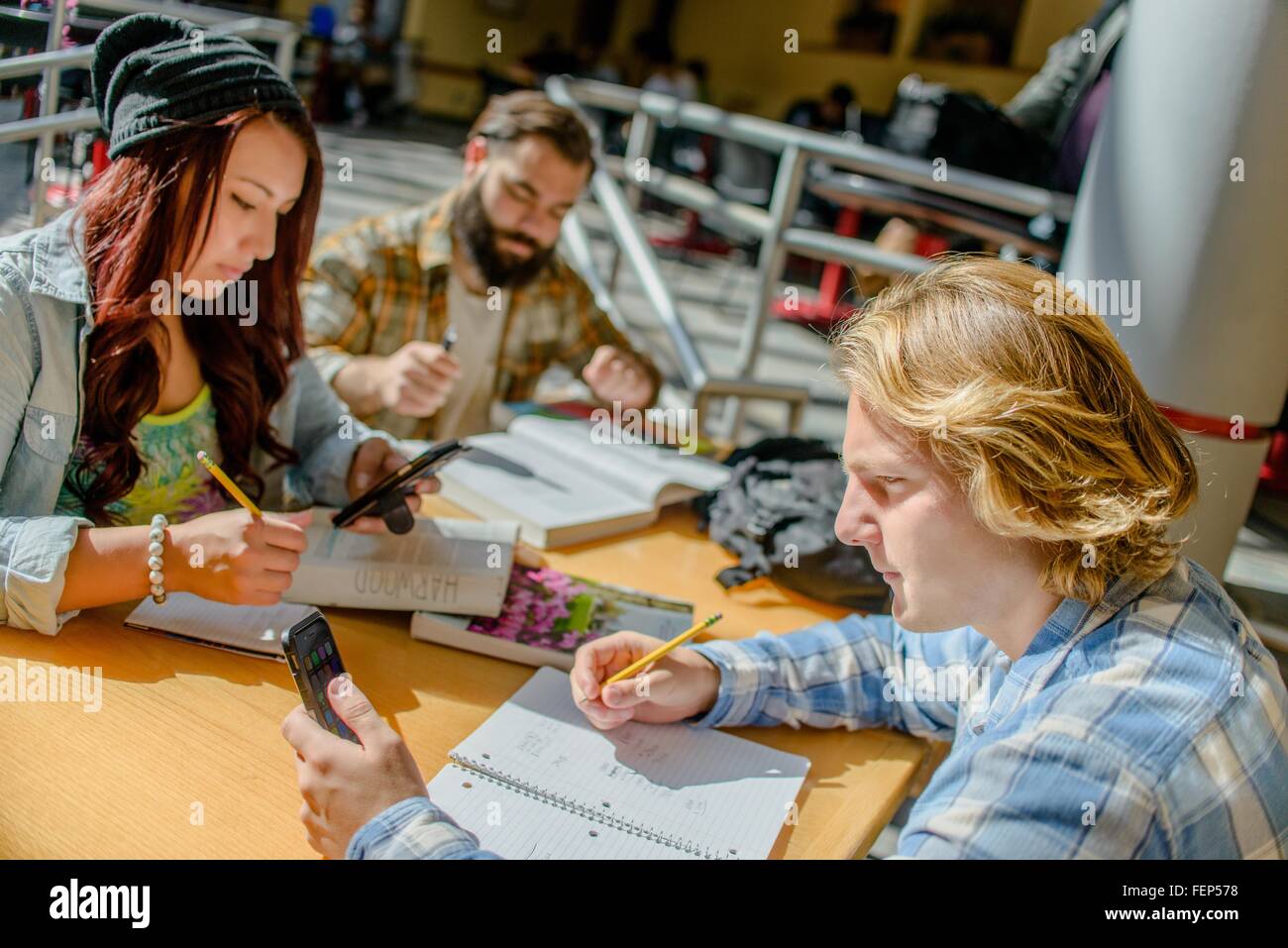Adulto di tre studenti del college rendendo note e tramite smartphone alla scrivania in aula Foto Stock