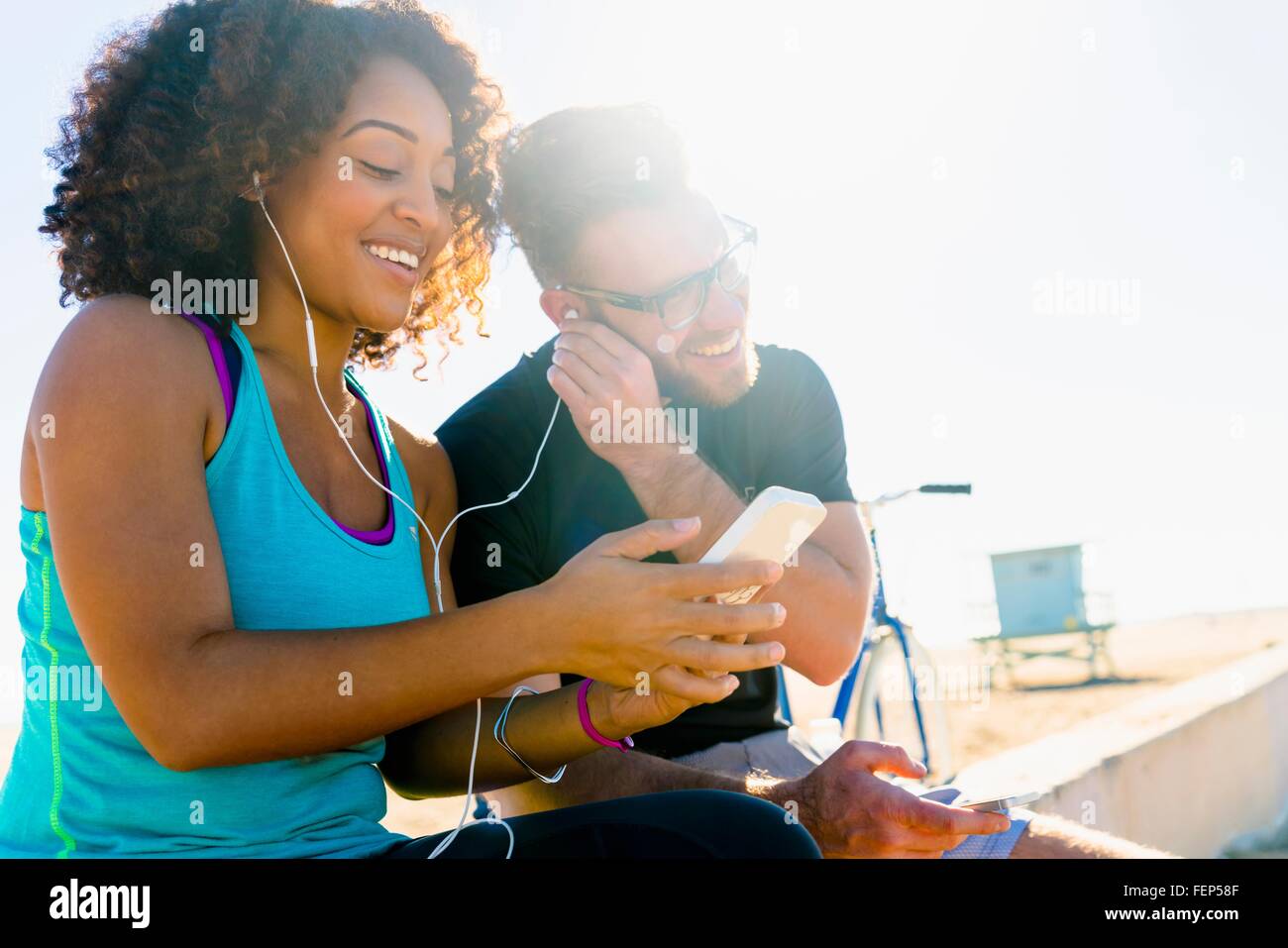 Giovane seduto sul muro, condividendo gli auricolari per ascoltare musica , utilizza lo smartphone Foto Stock
