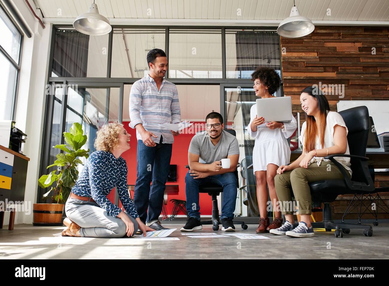Gruppo di persone creative a discutere di un nuovo progetto. Donna seduta con i documenti di cui sul pavimento e sorridere mentre avente un incontro che ho Foto Stock