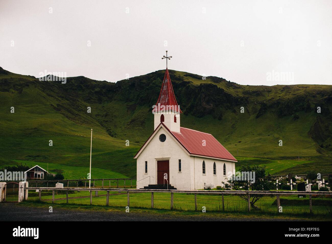 Villaggio Chiesa sotto verde e lussureggiante mountain range, Islanda Foto Stock