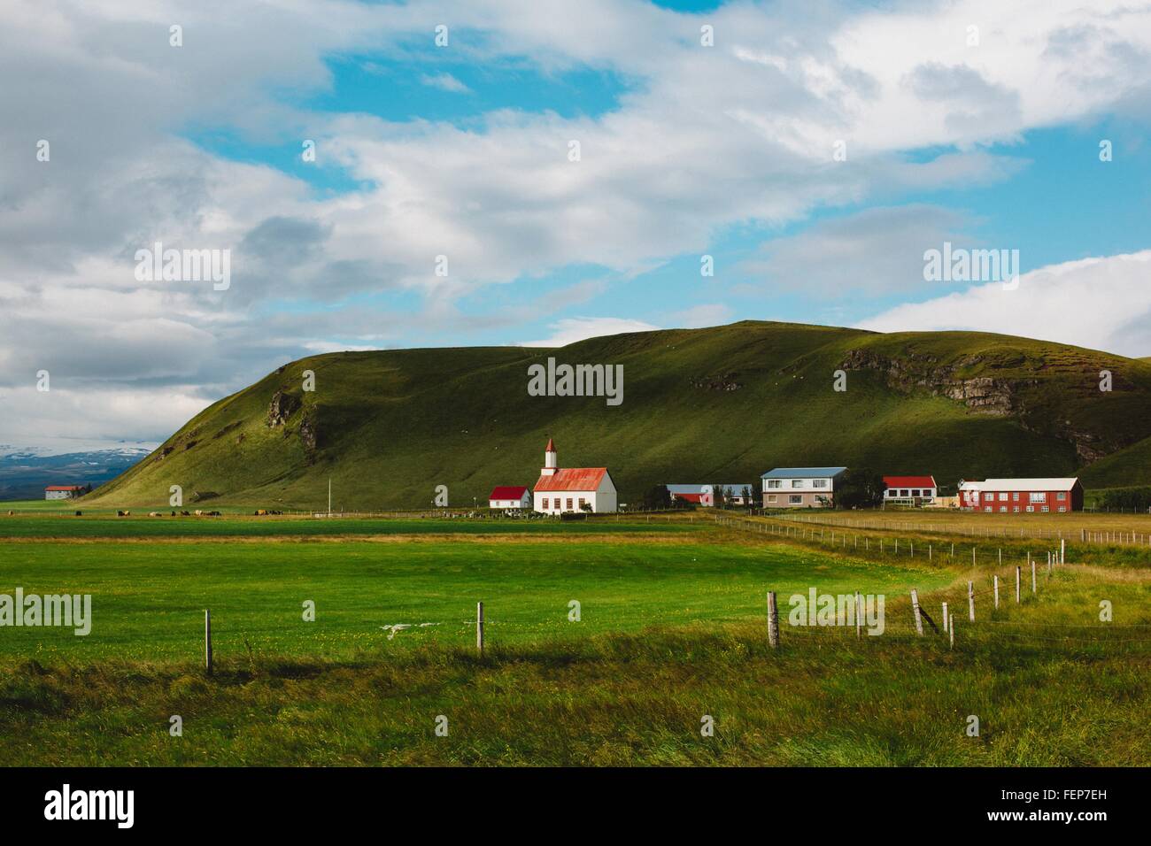 Remoto villaggio al di sotto di verde lussureggiante mountain range, Islanda Foto Stock