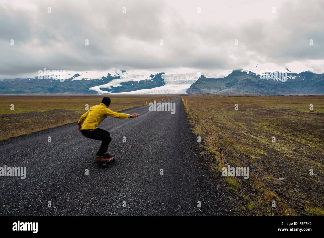Vista posteriore della metà uomo adulto lo skateboard di coperta di neve mountain range, Islanda Foto Stock