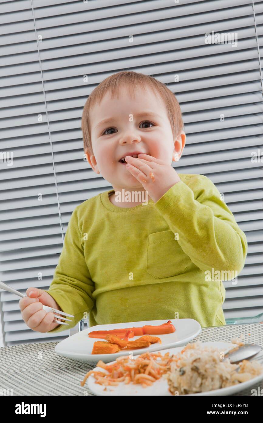 Baby boy alimentando lo stesso al tavolo da pranzo Foto Stock