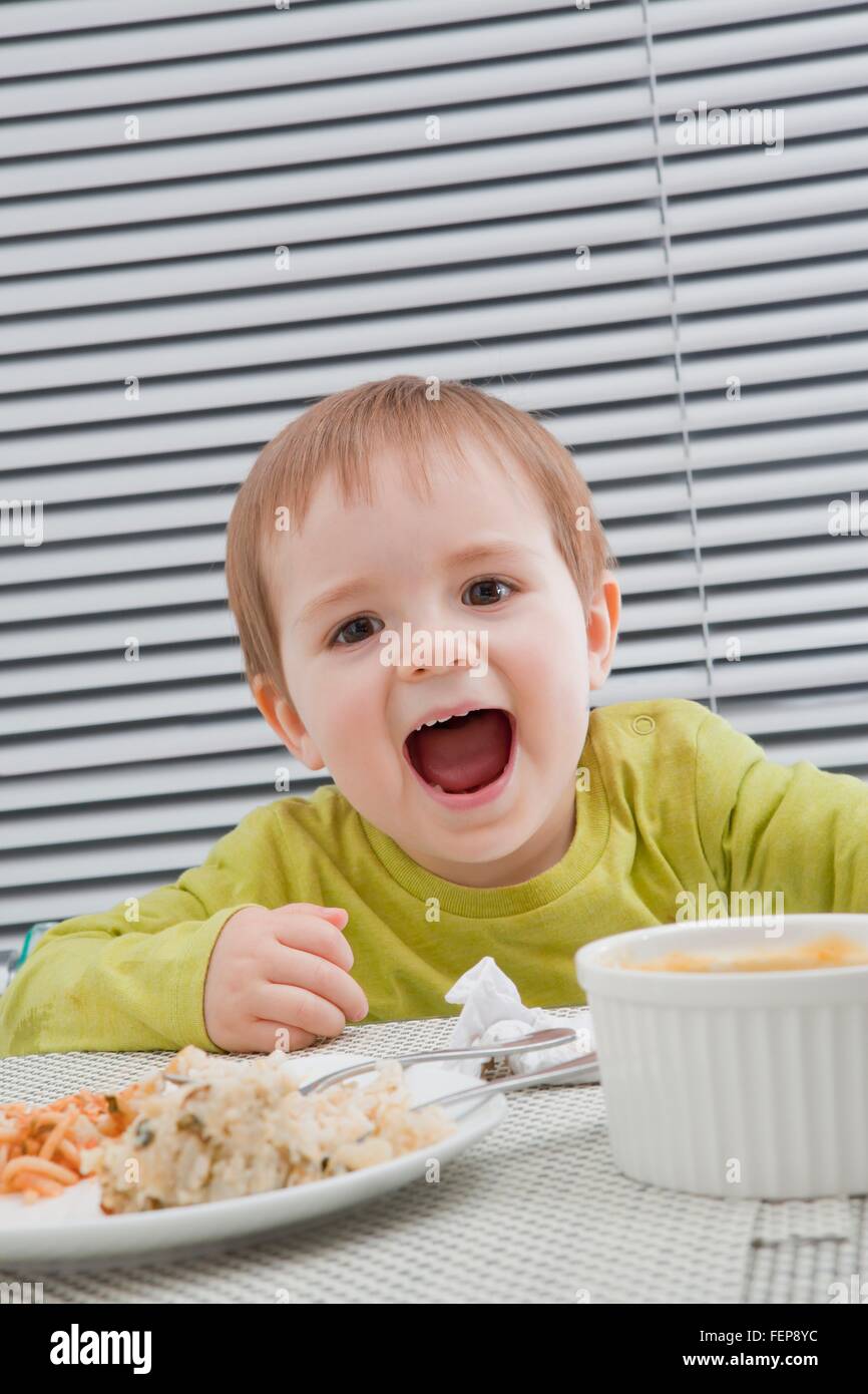Baby boy alimentando lo stesso al tavolo da pranzo Foto Stock